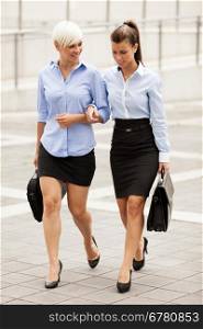 Two businesswoman are walking on the street while taling and laughing