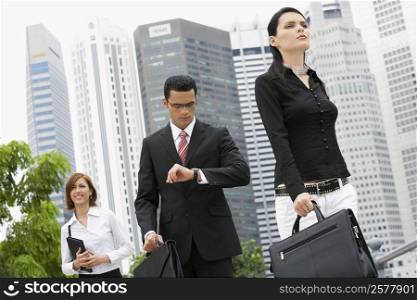 Two businesswomen and a businessman walking in front of buildings