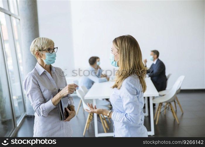 Two businesswomen, mature and young one, talking in the office and wearing mask as a virus protection