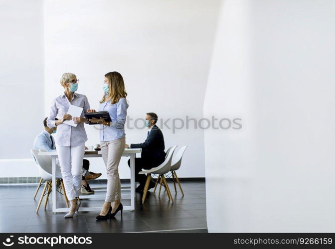 Two businesswomen, mature and young one, talking in the office and wearing mask as a virus protection