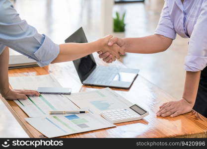 Two businesswomen shaking hands after reading paper and discussion deal agreement with new business.
