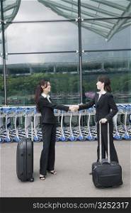 Two businesswomen shaking hands outside an airport