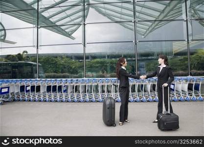 Two businesswomen shaking hands outside an airport