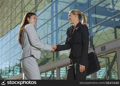 Two businesswomen shaking hands outside office building