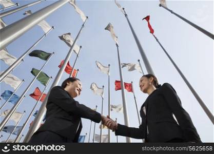 Two businesswomen shaking hands with flags in background.