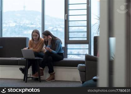 Two businesswomen sitting in a modern coworking space on a break from work and relaxing using a laptop. Selective focus. High-quality photo. Two business women sitingt in a modern coworking space on a break from work and relax using a laptop. Selective focus 