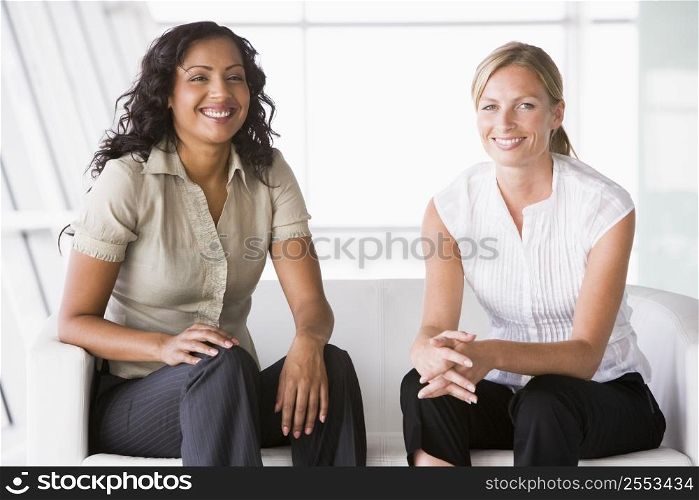 Two businesswomen sitting indoors smiling (high key/selective focus)