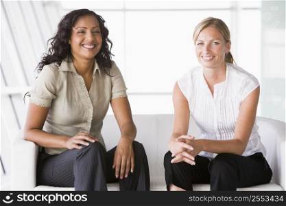 Two businesswomen sitting indoors smiling (high key/selective focus)