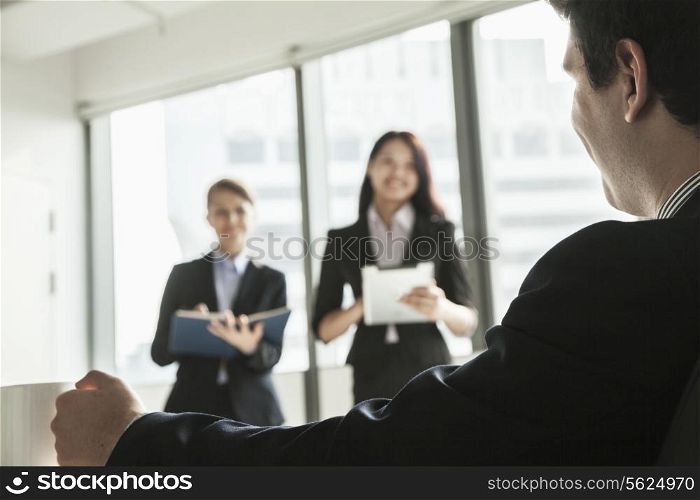 Two businesswomen standing up and presenting during a business meeting as a businessman watches