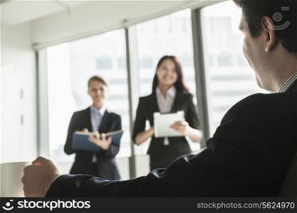 Two businesswomen standing up and presenting during a business meeting as a businessman watches