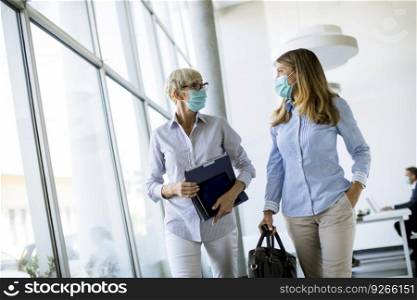 Two businesswomen walking in the office and wearing mask as a virus protection