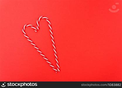 Two candy canes made making Heart of Christmas candies on red background with copy space