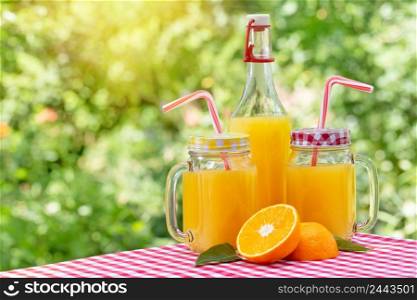Two cans and a bottle with orange juice on a red checkered tablecloth. Natural green background. Two cans and bottle with orange juice on red checkered tablecloth