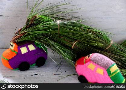 Two car transport pine tree for Xmas decoration, knitted colorful cars move on wooden make funny Christmas background
