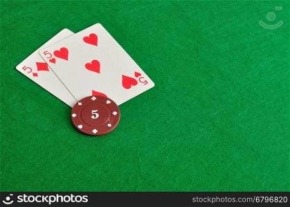 Two cards with a poker chip with the value of five on a green background
