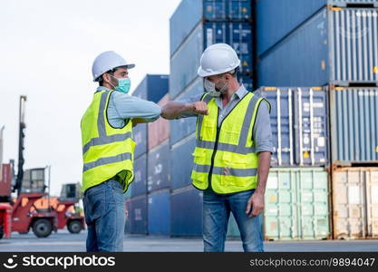 Two cargo container workers or engineer men show greeting together with new normal style by touching their elbow in workplace area. Concept of new normal lifestyle during pandemic of Covid-19 virus.