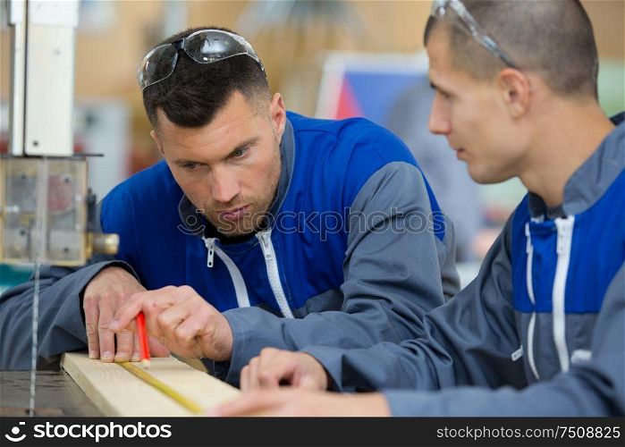 two carpenters are talking while holding papers and ruler