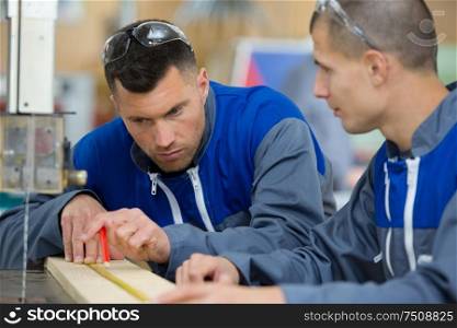 two carpenters are talking while holding papers and ruler