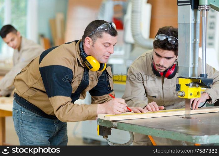 two carpenters in workshop measuring wood to saw