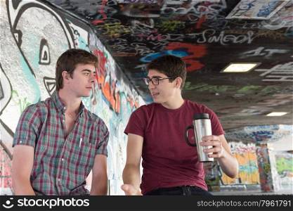 Two Casual Young Adults Drinking Coffee and Chatting in Graffiti Skate Park