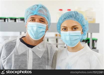 Two caucasian doctors or scientists at hospital or laboratory - Man and woman people wearing protective equipment mask and bouffant cap looking to the camera - protection and solution concept