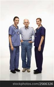 Two Caucasian females wearing scrubs standing with elderly Caucasian male.