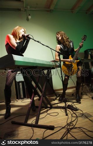 Two caucasian girls singing into microphone and playing the guitar.