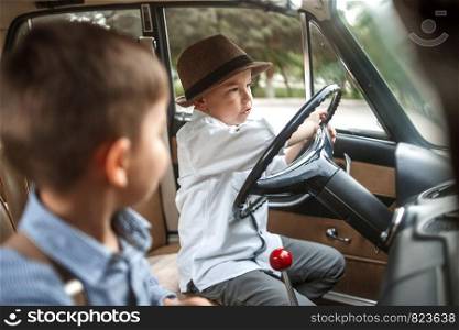 two Caucasian little boys in vintage clothes sitting inside a retro car
