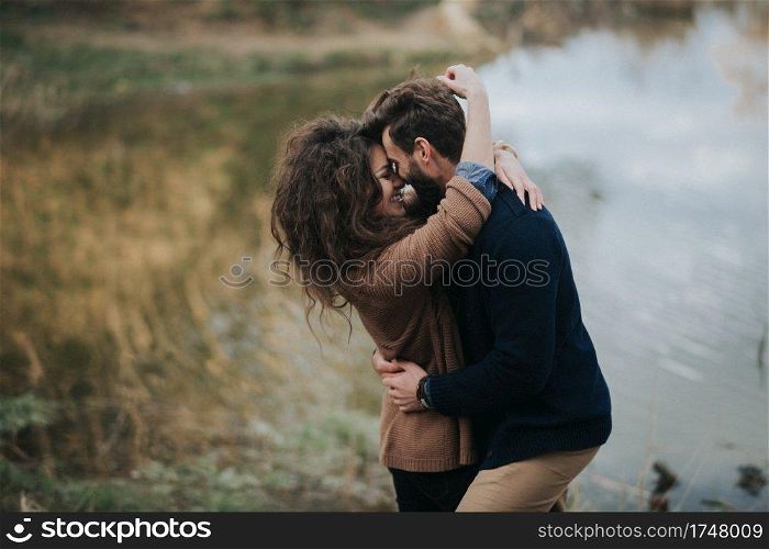 two caucasian lovers near the lake. Young couple is hugging on autumn day outdoors. A bearded man and curly woman in love. Valentine&rsquo;s Day. Concept of love and family.. two caucasian lovers near the lake. Young couple is hugging on autumn day outdoors. A bearded man and curly woman in love. Valentine&rsquo;s Day. Concept of love and family