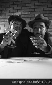 Two Caucasian prime adult males in retro suits sitting at table with martinis.