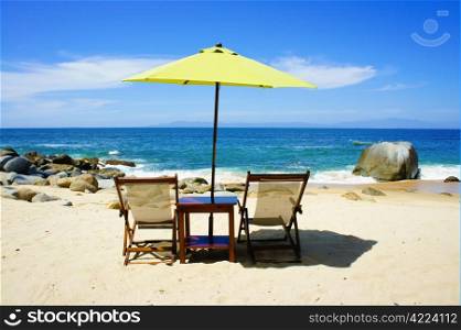 Two chairs a table and a yellow umbrella on the beach