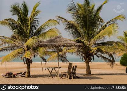 Two chairs and coffee table under a palm leaf and wood parasol on Bijilo Beach in The Gambia