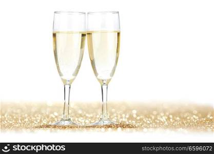 Two champagne glasses and golden shiny glitters isolated on white background