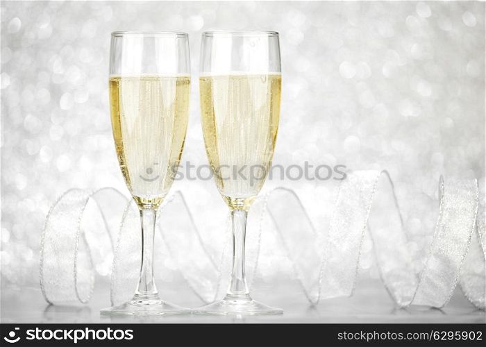 Two champagne glasses and ribbon on silver bokeh background