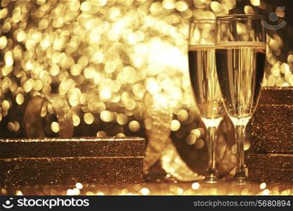 Two champagne glasses with gift boxes over shiny bokeh background
