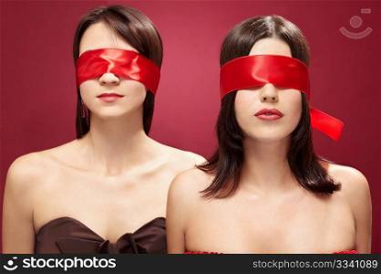 Two charming girls blindfold on a red background