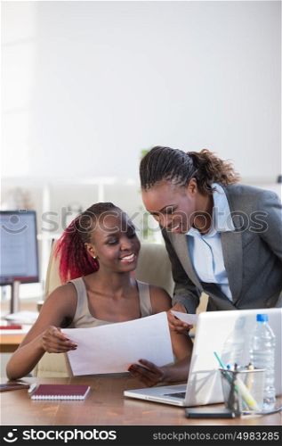 Two cheerful african american business women working at the office on a computer