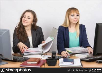 Two cheerful employee of the office sitting at a desk and working with documents