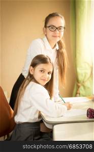 Two cheerful girls in school uniform posing behind desk