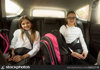 Two cheerful schoolgirls sitting on car back seat