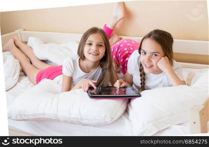 Two cheerful teenage girls lying on bed and using digital tablet