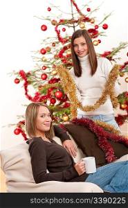 Two cheerful women with Christmas chains and balls in front of tree