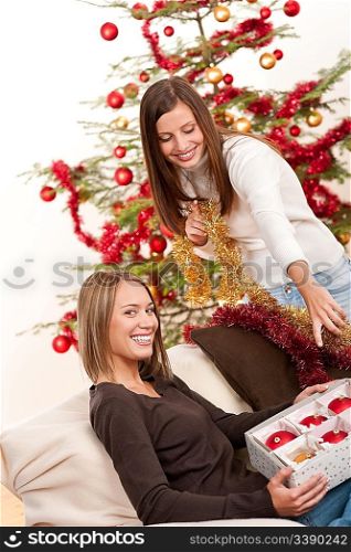 Two cheerful women with Christmas chains and balls in front of tree