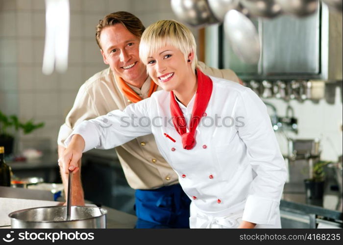 Two chefs in teamwork - man and woman - in a restaurant or hotel kitchen cooking delicious food