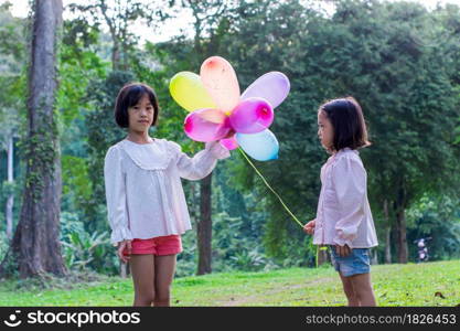 Two child girl holding colorful toy balloons in the park outdoors.