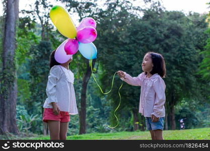 Two child girl holding colorful toy balloons in the park outdoors.