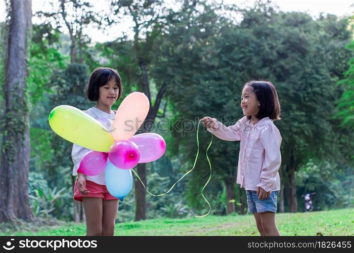 Two child girl holding colorful toy balloons in the park outdoors.