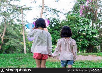 Two child girl holding colorful toy balloons in the park outdoors.