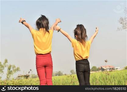Two child girls in a field and their hands are raised up to the sky
