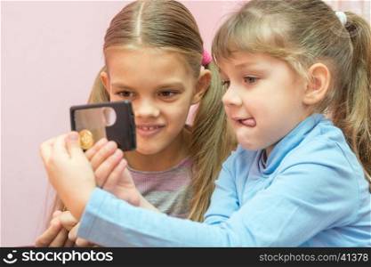 Two children considered a coin through a magnifying glass